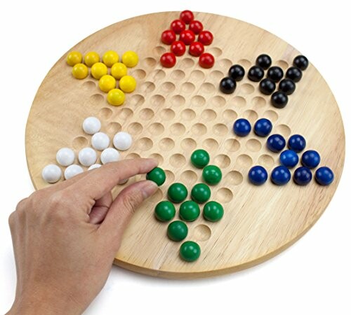 Hand playing Chinese checkers with colorful marbles on a wooden board.